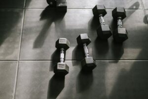 pexels photo 16513597 16513597 Hexagonal dumbbells on a gym floor bathed in natural sunlight, creating dynamic shadows.