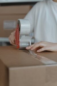 pexels photo 6169019 6169019 A person sealing a cardboard box with a tape dispenser in an indoor setting.