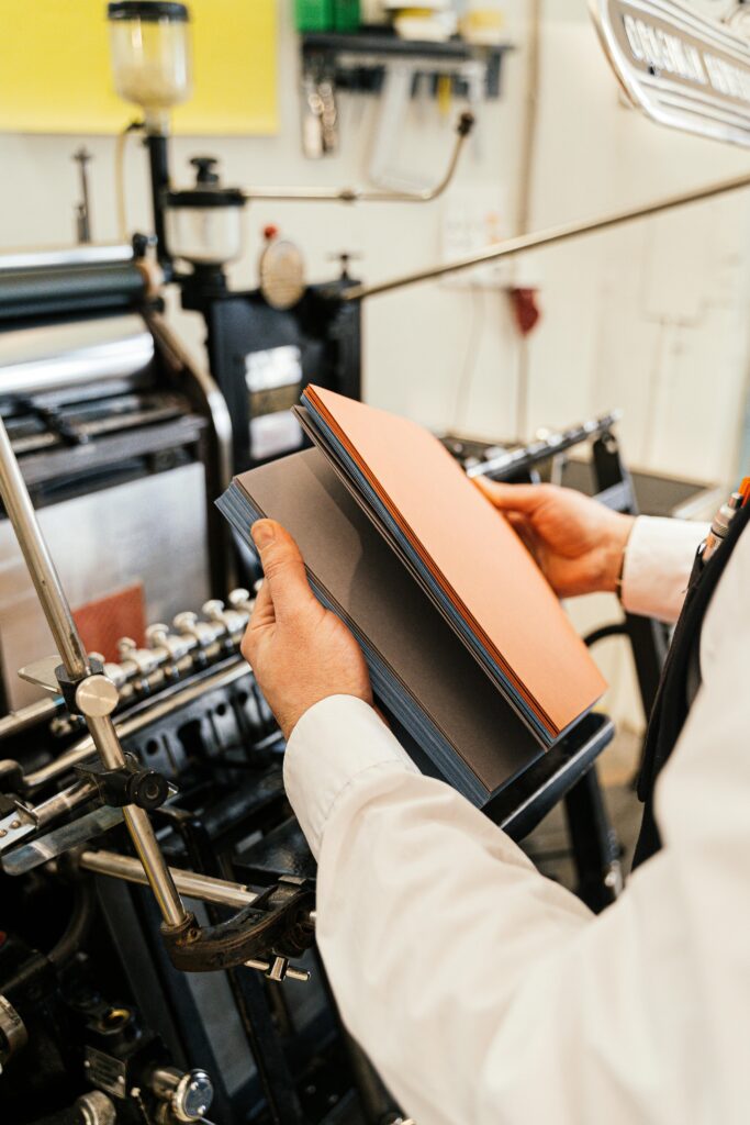 pexels photo 6620970 6620970 Person holding papers near a printing press in a workshop setting.