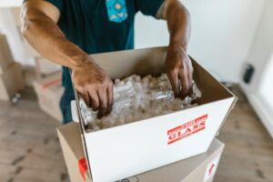 pexels photo 7464674 7464674 Hands carefully packing glassware into a cardboard box with padding for safe transport.